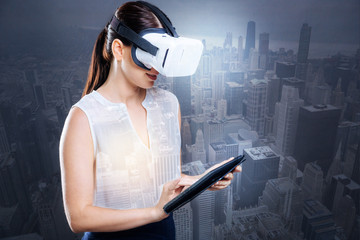 Pleasant businesswoman using tablet while wearing VR goggles