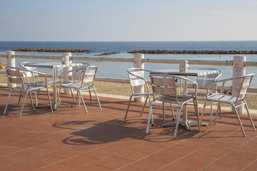Sedie e tavolini d'acciaio fuori un bar in un piccolo paese vicino il mare. Non c'è nessuno seduto ai tavoli.
