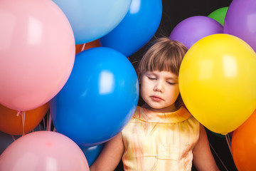 Sad blond little girl with colorful balloons