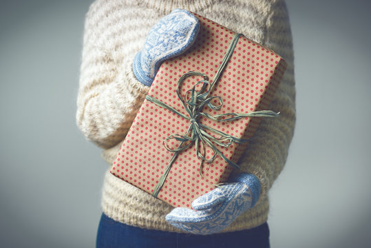 Christmas background. Girl in a warm knitted sweater and mittens is holding a Christmas present. Gifts for men. Merry Christmas. Gift for a girl. Knitted dress. Image is toned in fashionable color.