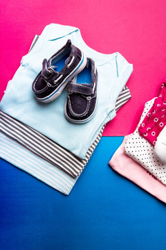Folded blue and pink bodysuit with boat shoes on it on minimalistic pink and blue background. diaper for newborn boy and girl. Stack of infant clothing. Child outfit. Top view.