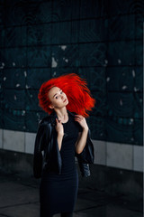 Fototapeta premium Expressive Redhead woman posing at dark wall and her hair flying against black background