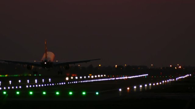 Big plane landing at Barcelona airport seen from behind at night with lit signal lights on the runway. 