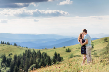 Fototapeta na wymiar Tender hugs of a couple standing on a green hill before gorgeous landscape