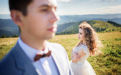 Wind blows bride's hair while she stands behind groom on the hill