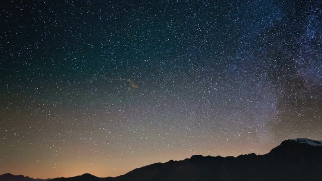 Scenic meteor explosion with stardust during time lapse of the Milky Way and the starry sky rotating over the Alps.