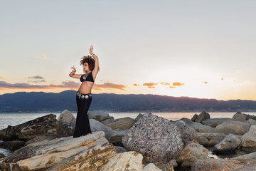 ragazza danza sugli scogli al tramonto in riva al mare