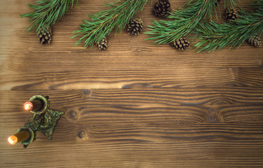 Fir tree branches with scattered cones around and candles in vintage candleholder on brown wooden table surface background with copy space. Christmas table decoration.