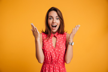 Photo of happy excited amazed young woman in red dress standing with open palms, looking at camera