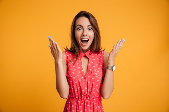 Photo Of Happy Excited Amazed Young Woman In Red Dress Standing With Open Palms, Looking At Camera