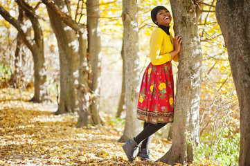 African american girl at yellow and red dress at golden autumn fall park.