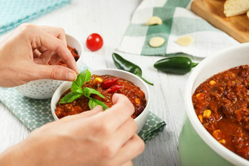 Woman decorating tasty chili con carne with basil leaves on table
