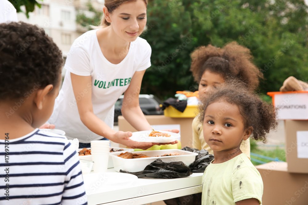 Wall mural Volunteer sharing food with poor African children outdoors