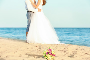 Fototapeta na wymiar Beautiful bouquet and happy wedding couple on sea beach