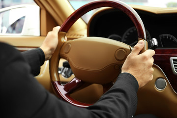 Young man holding hands on steering wheel of car