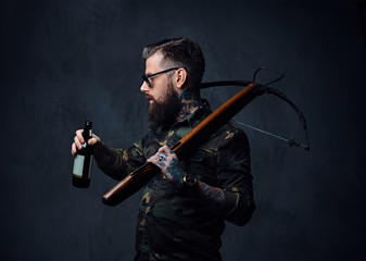 Fototapeta premium A man holds the craft beer bottle and a crossbow.