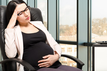 Tired  beautiful pregnant woman at workplace in the office