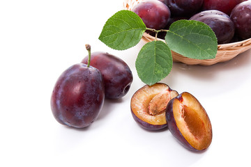 Yellow wooden basket with ripe plums, whole and half ripe plums isolated on a white background..