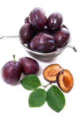 Steel colander with ripe plums, whole and half ripe plums with leaf isolated on a white background..