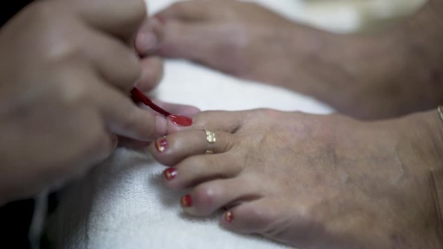 Very tight shot of a mature woman’s foot with ankle chain and toe ring, while getting her toenails painted.
