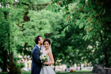 Handsome groom and pretty bride with white bouquet stand on green lawn