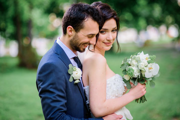 Groom hugs stunning brunette bride tender posing in the park