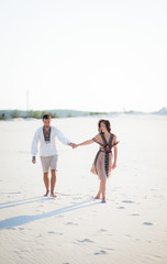 Barefooted couple in bright embroidered clothing walks on a white sand