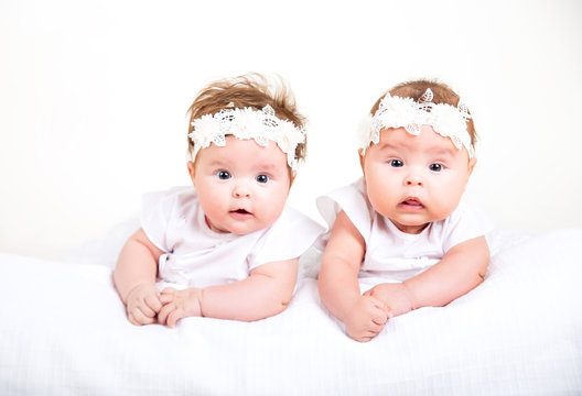 Two cute kids lying on the white background. Portrait of twins in white gowns and bandages on their heads on a white background