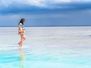 Fototapeta na wymiar A girl walks along the surface of a salt lake at a spa resort. Young woman on the beach with white sand and beautiful scenery around