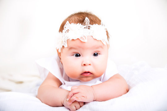 cute kid lying on the white background. Portrait of baby in white gown and bandage on her head on a white background