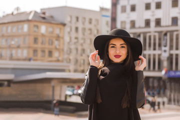 Obraz premium Lifestyle portrait of beautiful brunette model with bright makeup in fashionable coat and hat posing at the city street