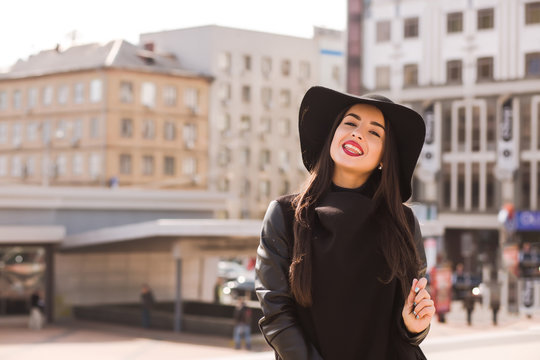 Lifestyle portrait of sexy brunette model with bright makeup in fashionable coat and hat posing at the city street