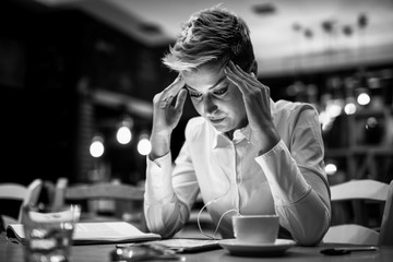 Fototapeta premium Stressed young woman entrepreneur sitting at the table with business plans and a cup of coffee.Black and white.