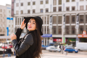 Fototapeta na wymiar Lifestyle portrait of smiling brunette model in fashionable coat and hat posing at the city street