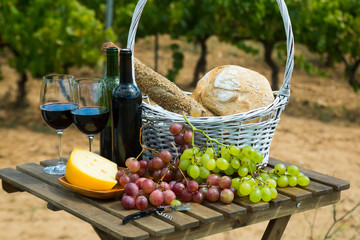 Red wine with cheese, bread in basket and grapes