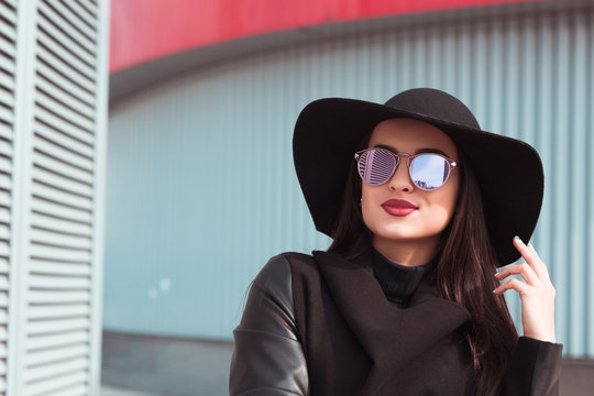 Closeup portrait of young model wears hat and sunglasses posing at sunny day. Female fashion concept
