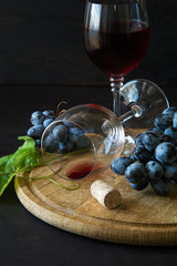 Two wineglasses with red wine and grapes decorated vine leaves on dark wooden desk