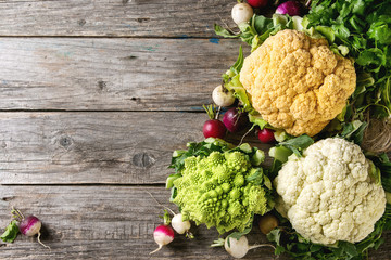 Variety of fresh raw organic colorful cauliflower, cabbage romanesco and radish with bundle of coriander over old wooden background. Top view with copy space. Food farm market concept © Natasha Breen