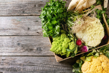Variety of fresh raw organic colorful cauliflower, cabbage romanesco and radish with bundle of coriander in wood box over old wooden background. Top view with copy space. Food farm market concept