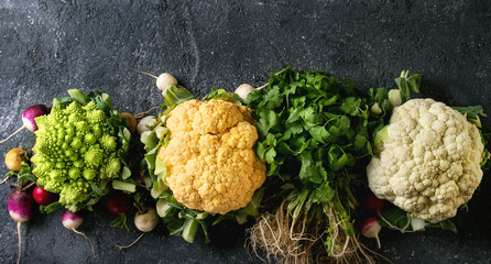 Variety of fresh raw organic colorful cauliflower, cabbage romanesco and radish with bundle of coriander over dark texture background. Top view with space. Banner. Healthy eating concept