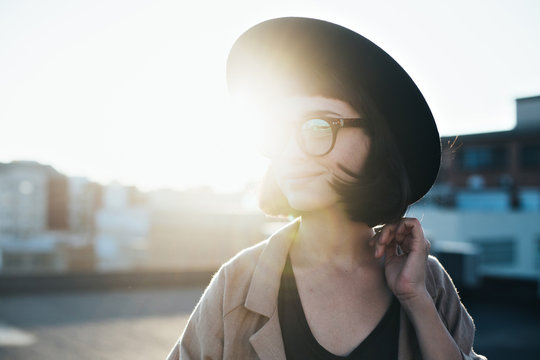 Beautiful natural beauty woman smiles and laughs shy and pretty, poses for camera on rooftop during sunset hours, in cute hipster outfit ang glasses