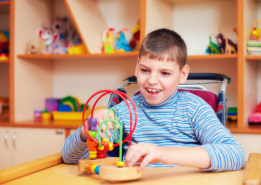 cheerful boy with disability at rehabilitation center for kids with special needs, solving logical puzzle