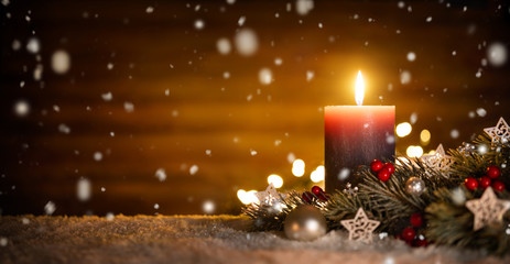 Kerze mit festlicher Dekoration und Holz Hintergrund bei fallendem Schnee, ideal für Advent und Weihnachten - obrazy, fototapety, plakaty