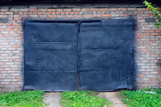Old painted black paint on garage in nature. Black door in a building against a brick wall. A green lawn path leads to the door.