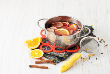 Cooked mulled wine in a saucepan, sieve, oranges and cinnamon