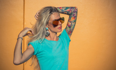 Beautiful blonde in sunglasses posing at the camera. Portrait on the background of bright orange...