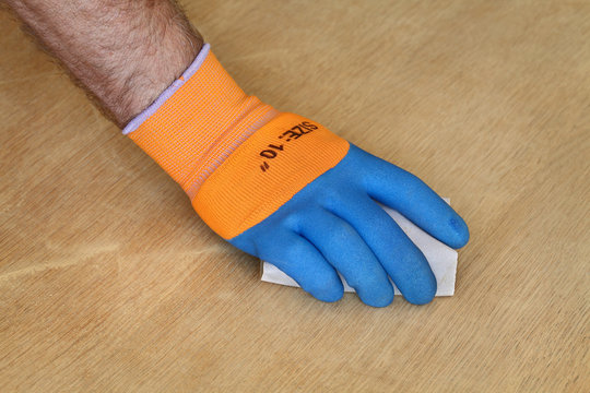 Closeup Of Worker Hand In Protective Glove Sanding Wooden Plank