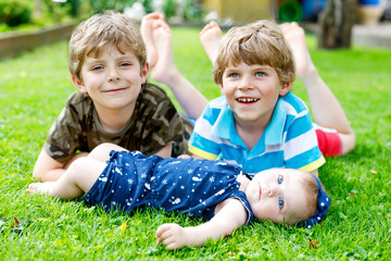 Two little happy kid boys with newborn baby girl, cute sister.