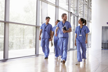 Four healthcare workers in scrubs walking in corridor - obrazy, fototapety, plakaty