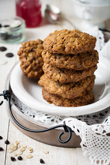 Stack of oatmeal cookies with chocolate on a light background with flakes and a bottle of milk. Selective focus.